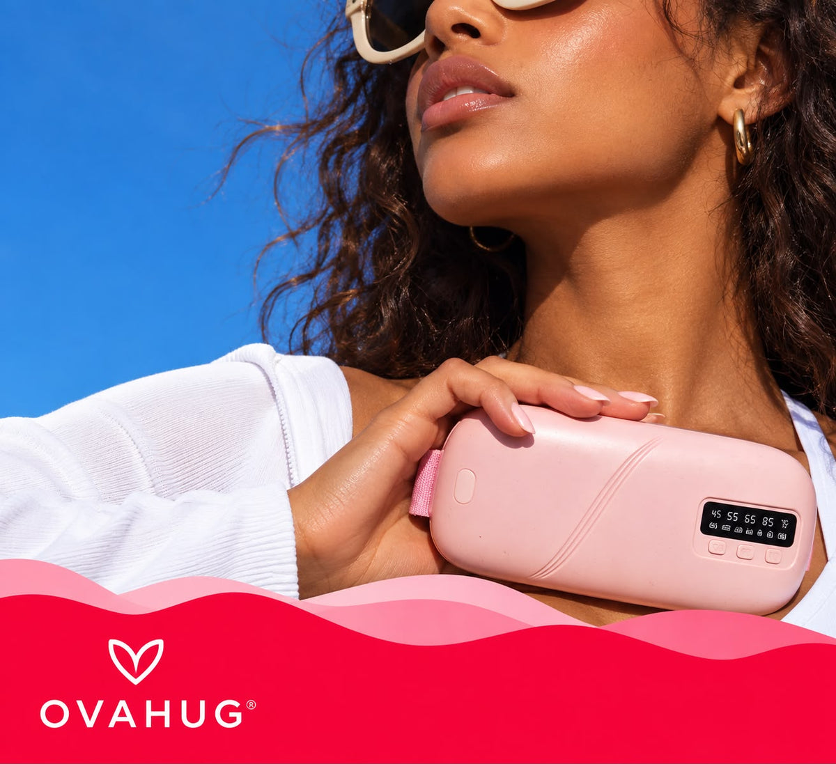 Woman holding the pink Ovahug heat and massage pad in the sun